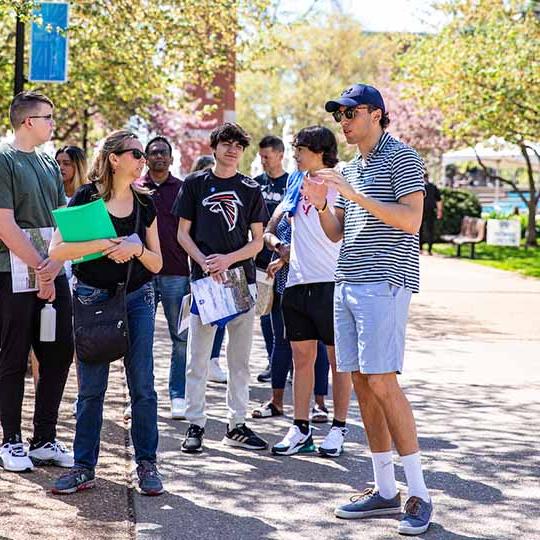 Group of students standing with a tour leader near the clock tower during a campus visit